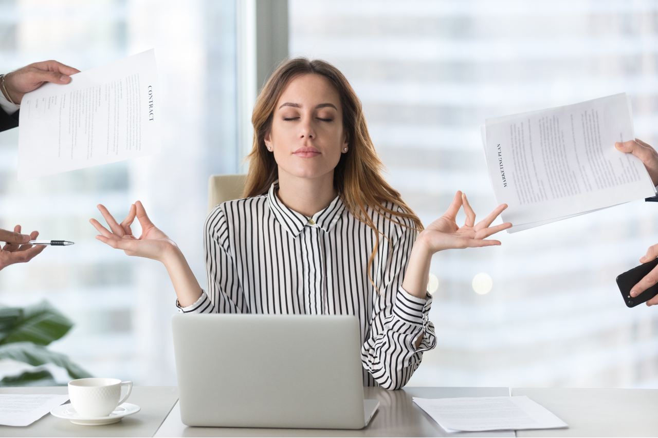 Woman practicing mindfulness meditation at desk to manage pressure and tension at work.
